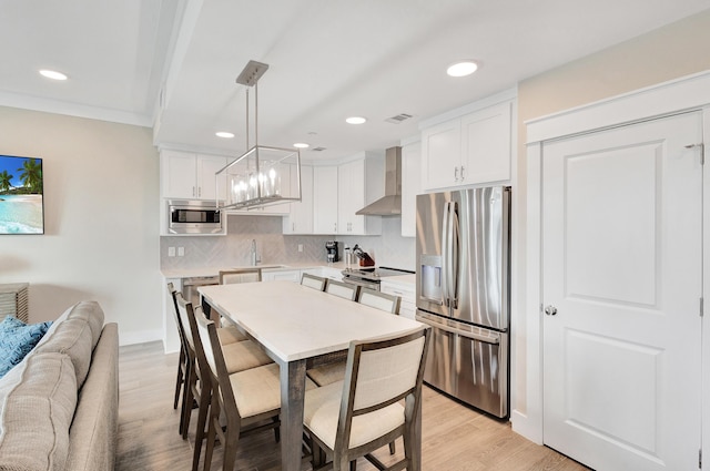 kitchen with pendant lighting, white cabinetry, sink, stainless steel appliances, and wall chimney exhaust hood