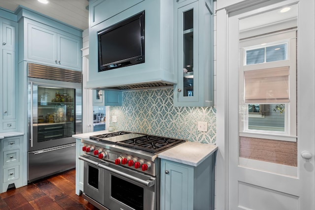 kitchen with premium appliances, dark wood finished floors, light countertops, decorative backsplash, and glass insert cabinets