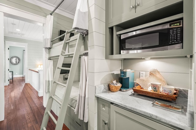 kitchen with dark wood finished floors, visible vents, stainless steel microwave, wooden walls, and light stone countertops