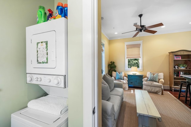 washroom with crown molding, a ceiling fan, stacked washer / dryer, wood finished floors, and laundry area