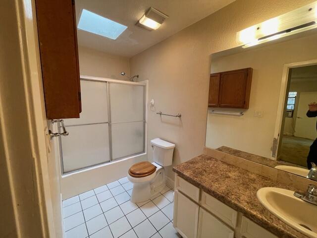 full bathroom featuring combined bath / shower with glass door, tile patterned flooring, a skylight, vanity, and toilet