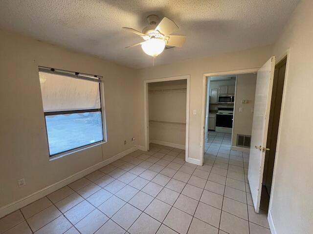 unfurnished bedroom with light tile patterned flooring, a textured ceiling, ceiling fan, and a closet