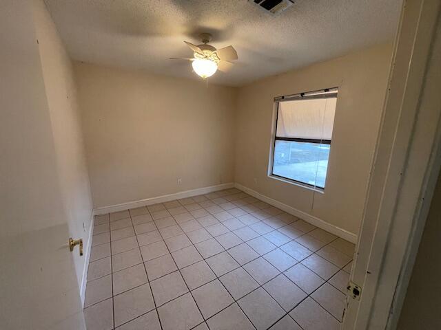 tiled empty room featuring ceiling fan and a textured ceiling