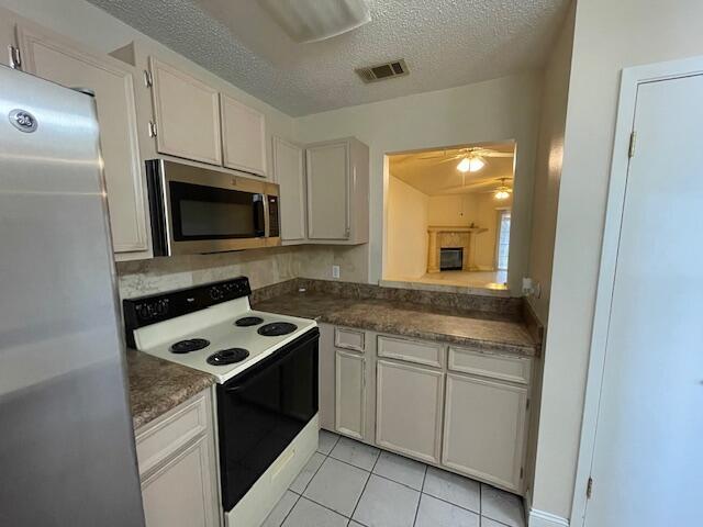 kitchen with ceiling fan, appliances with stainless steel finishes, white cabinetry, a textured ceiling, and light tile patterned flooring