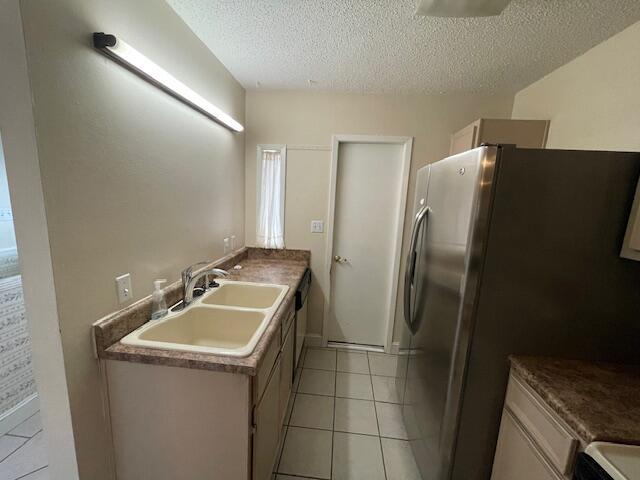 kitchen featuring sink, stainless steel refrigerator, a textured ceiling, and light tile patterned flooring