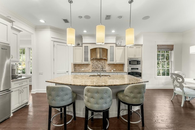 kitchen featuring dark wood-type flooring, a sink, backsplash, appliances with stainless steel finishes, and wall chimney range hood