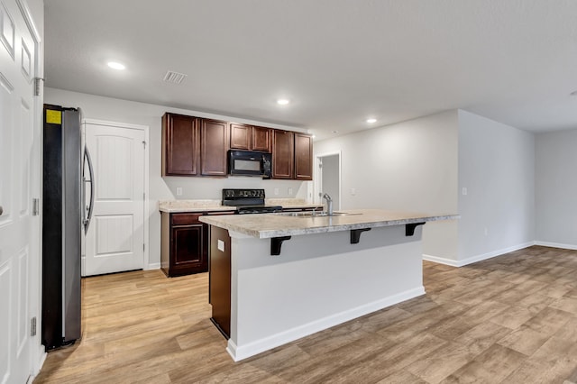 kitchen with a kitchen bar, sink, light wood-type flooring, a kitchen island with sink, and black appliances