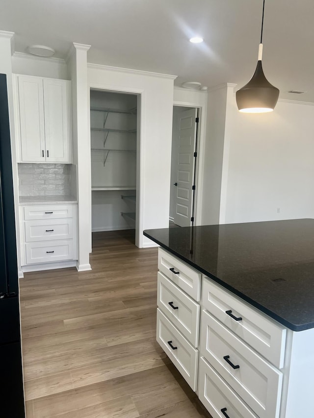 kitchen featuring white cabinetry, light wood-type flooring, ornamental molding, decorative backsplash, and pendant lighting