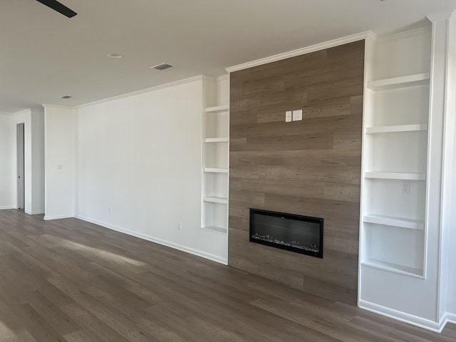 unfurnished living room featuring crown molding, a large fireplace, built in features, and dark hardwood / wood-style floors