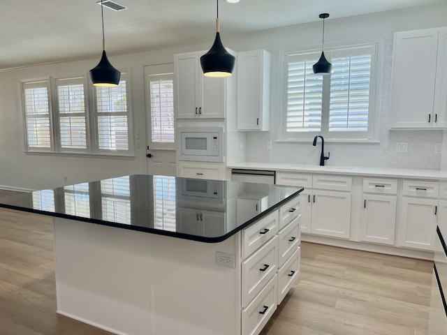 kitchen with sink, white cabinetry, pendant lighting, a kitchen island, and white microwave