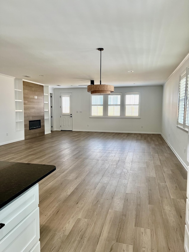 unfurnished living room featuring light wood-type flooring, a tiled fireplace, and plenty of natural light