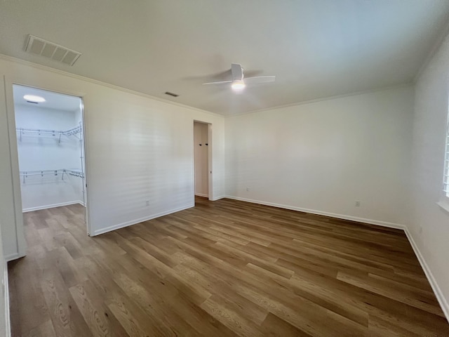 unfurnished bedroom featuring crown molding, a walk in closet, wood-type flooring, and ceiling fan