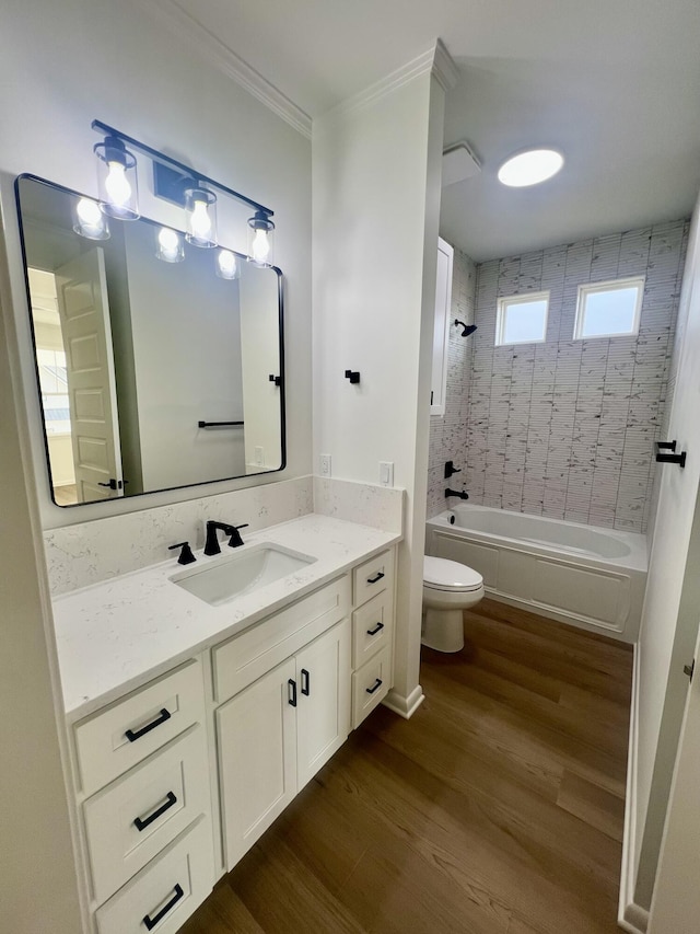 full bathroom featuring vanity, tiled shower / bath combo, toilet, hardwood / wood-style flooring, and ornamental molding