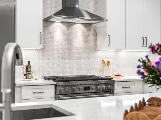 kitchen with wall chimney range hood, white cabinets, high end stove, and tasteful backsplash