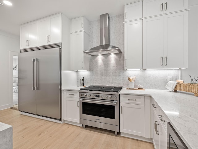 kitchen featuring wall chimney range hood, high end appliances, backsplash, and white cabinets