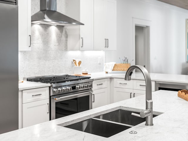 kitchen with sink, appliances with stainless steel finishes, white cabinetry, and wall chimney exhaust hood