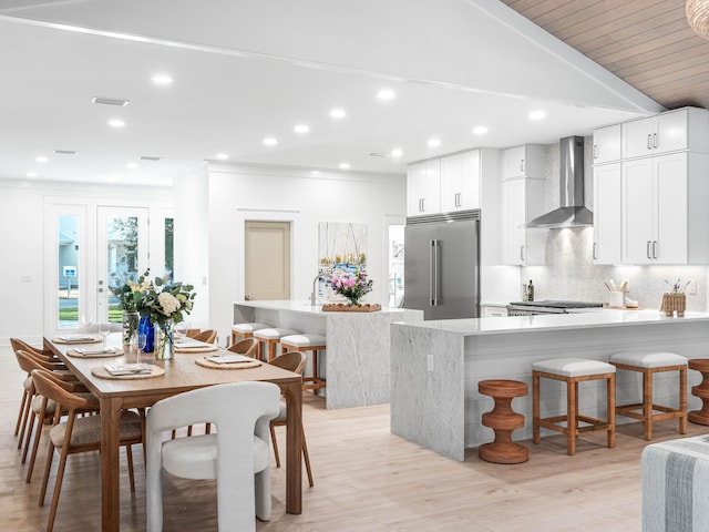 kitchen featuring white cabinetry, wall chimney range hood, a breakfast bar area, and stainless steel built in refrigerator