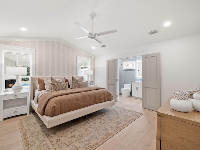 bedroom with ceiling fan, lofted ceiling, connected bathroom, and light hardwood / wood-style flooring