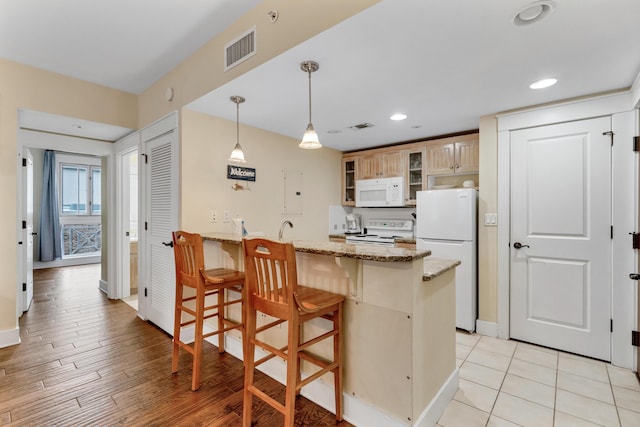 kitchen featuring white appliances, a kitchen bar, kitchen peninsula, hanging light fixtures, and light stone countertops