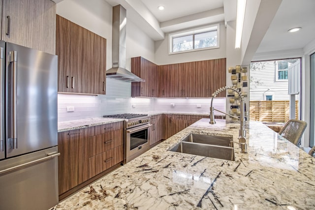 kitchen featuring sink, backsplash, premium appliances, light stone countertops, and wall chimney exhaust hood