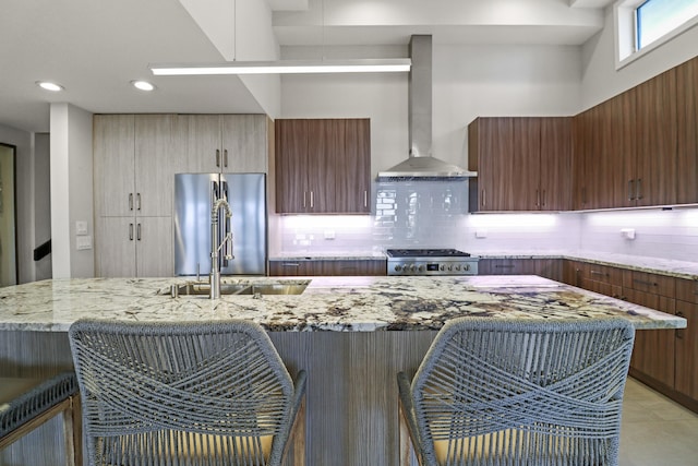 kitchen featuring wall chimney exhaust hood, range, stainless steel refrigerator, light stone countertops, and decorative backsplash