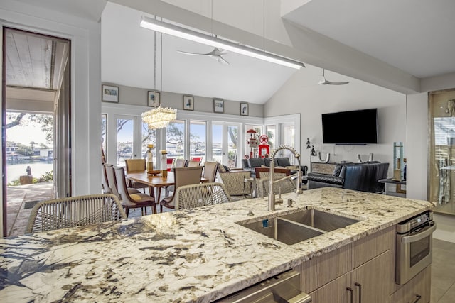 kitchen with vaulted ceiling, sink, ceiling fan, light stone counters, and a water view