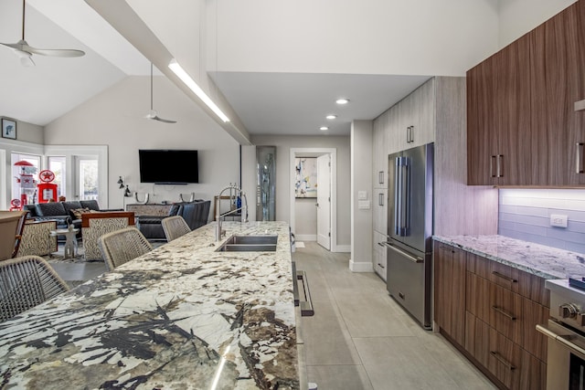 kitchen featuring a breakfast bar, sink, light stone counters, high end refrigerator, and ceiling fan