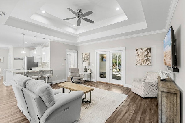 living room featuring french doors, ornamental molding, a raised ceiling, hardwood / wood-style flooring, and ceiling fan