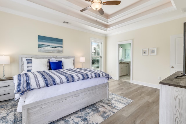 bedroom with crown molding, ceiling fan, connected bathroom, a tray ceiling, and light wood-type flooring