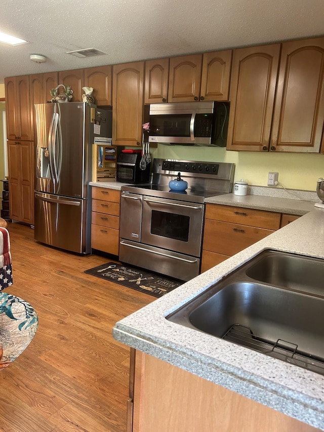 kitchen with stainless steel appliances, sink, light hardwood / wood-style flooring, and a textured ceiling