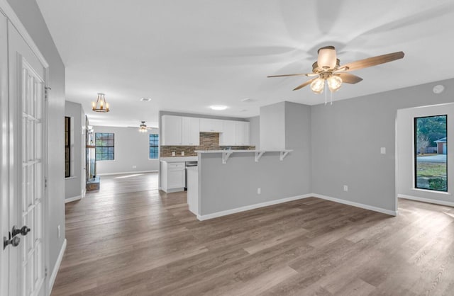 unfurnished living room with ceiling fan with notable chandelier and light wood-type flooring