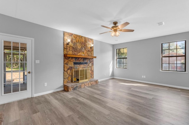 unfurnished living room featuring hardwood / wood-style flooring, ceiling fan, and a stone fireplace