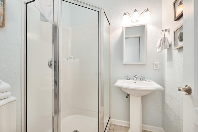 bathroom with a textured wall, a sink, baseboards, a shower stall, and tile patterned floors