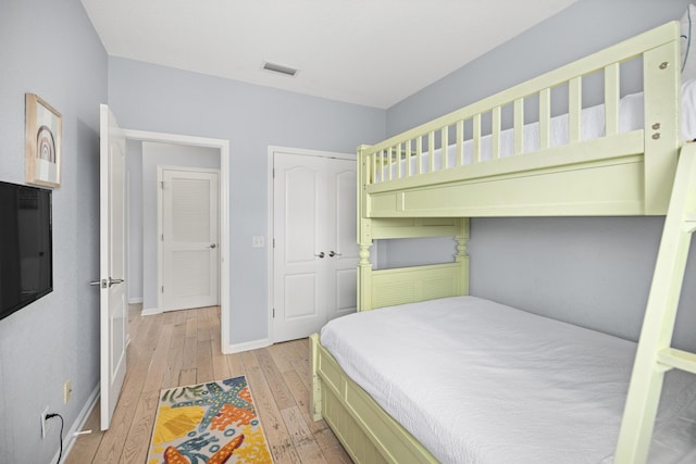 bedroom with a closet, visible vents, light wood-style flooring, and baseboards