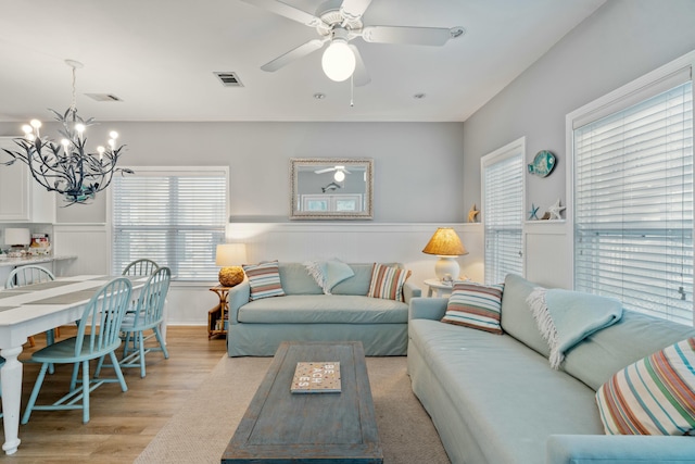 living room featuring ceiling fan with notable chandelier and light hardwood / wood-style flooring