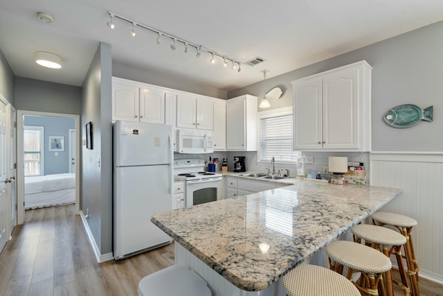 kitchen with a breakfast bar, sink, decorative light fixtures, white appliances, and white cabinets