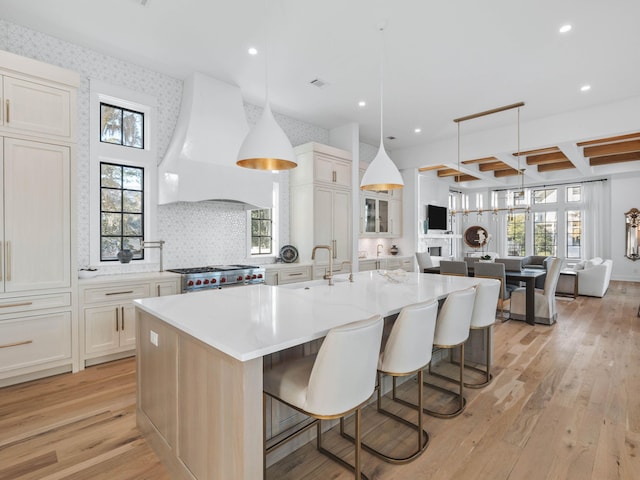 kitchen with premium range hood, pendant lighting, a breakfast bar area, a large island with sink, and range with two ovens