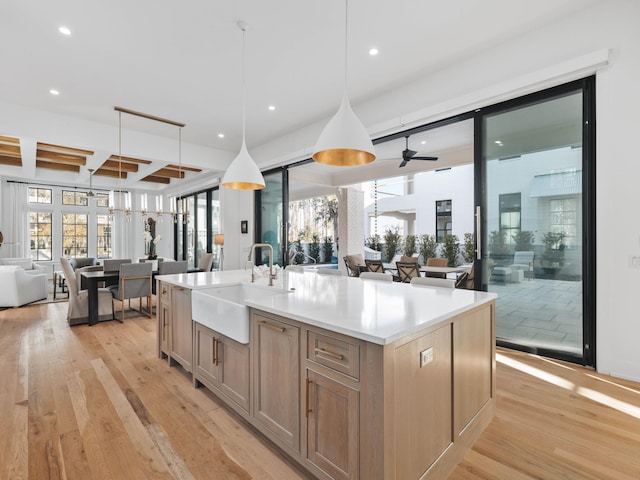 kitchen featuring sink, decorative light fixtures, light hardwood / wood-style floors, and an island with sink