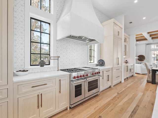 kitchen featuring tasteful backsplash, custom range hood, beam ceiling, light hardwood / wood-style floors, and range with two ovens