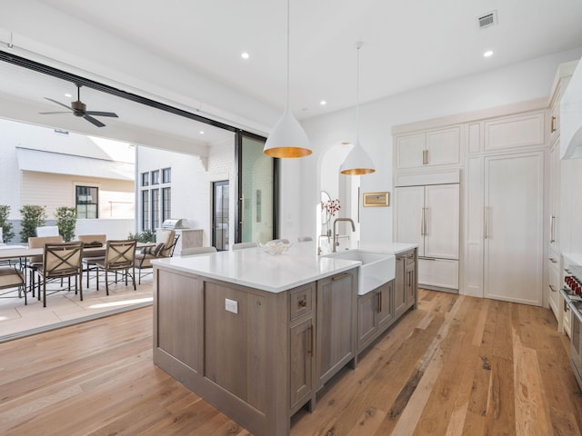 kitchen featuring sink, decorative light fixtures, light hardwood / wood-style flooring, paneled built in refrigerator, and an island with sink