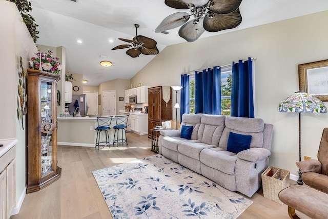 living room with ceiling fan, vaulted ceiling, and light wood-type flooring