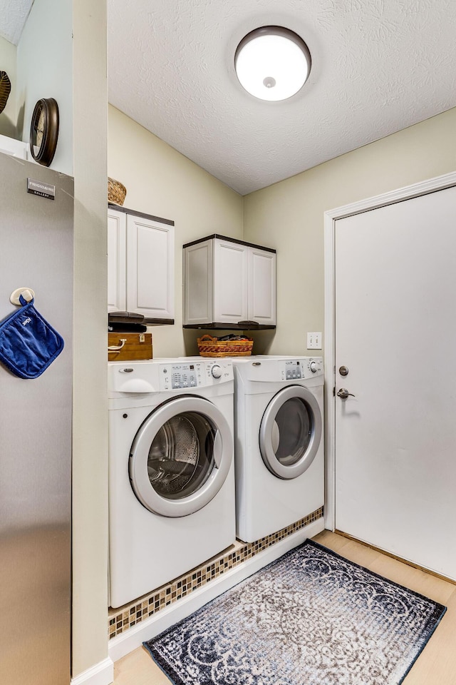 laundry area with cabinets, washing machine and clothes dryer, and a textured ceiling