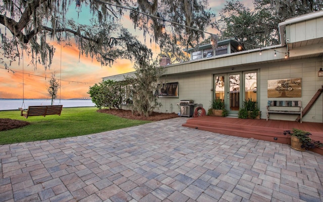 patio terrace at dusk featuring a water view, a yard, and grilling area