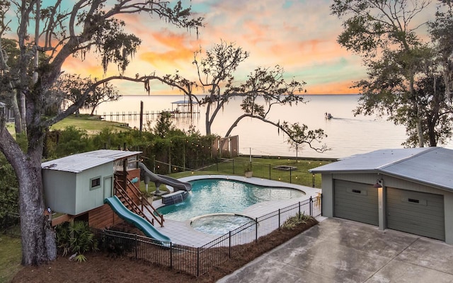 pool at dusk with a water slide, an outbuilding, a water view, a playground, and a garage