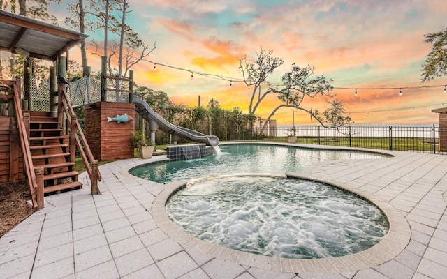 pool at dusk with a patio area, an in ground hot tub, and a water slide