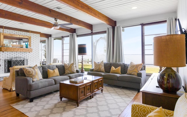 living room with beamed ceiling, plenty of natural light, light hardwood / wood-style floors, and a brick fireplace