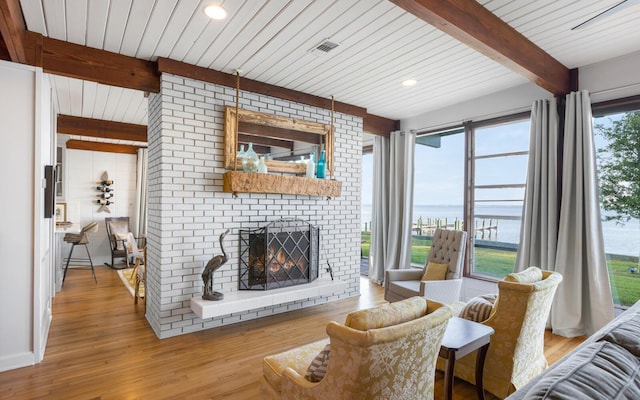 living room featuring a water view, beamed ceiling, a brick fireplace, and light wood-type flooring