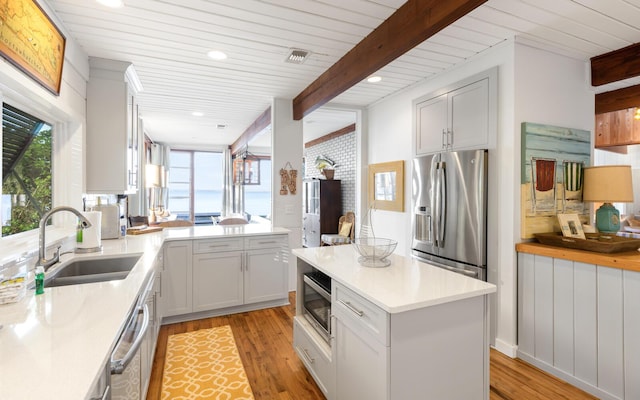 kitchen featuring sink, light hardwood / wood-style floors, beamed ceiling, and appliances with stainless steel finishes