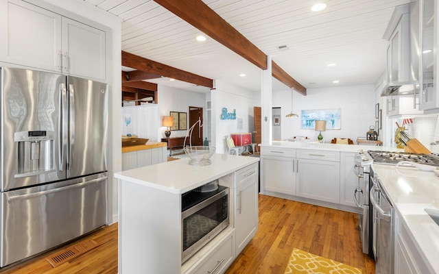 kitchen featuring wall chimney range hood, appliances with stainless steel finishes, beam ceiling, a center island, and light hardwood / wood-style floors