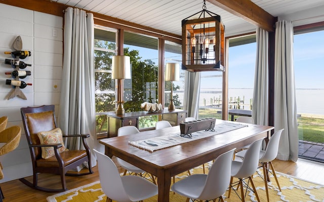 dining space with a water view, beamed ceiling, a chandelier, and light wood-type flooring